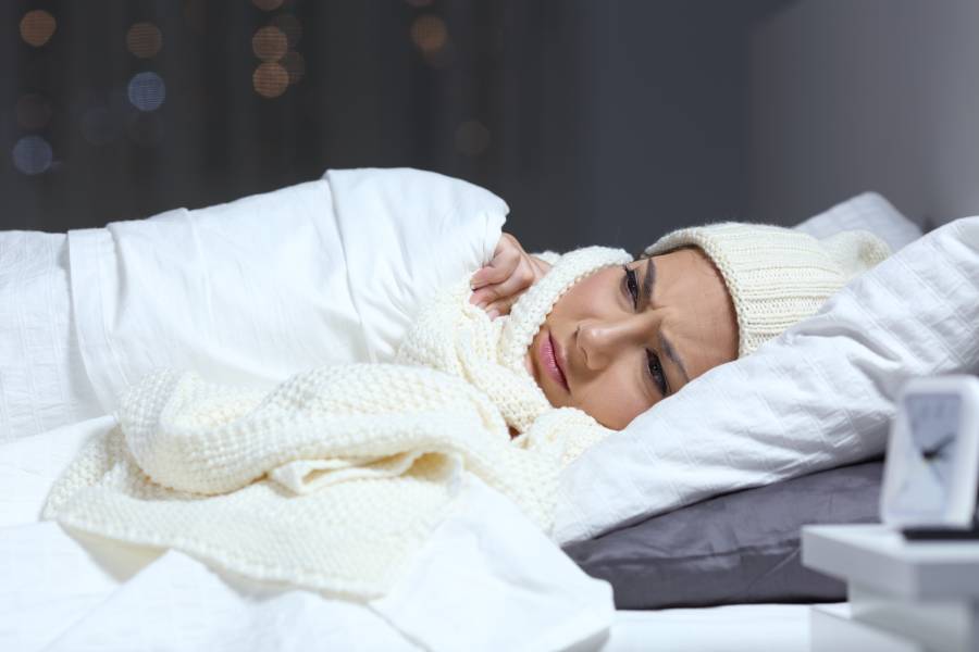 Woman bundled in bed contemplating how long she can leave her space heater on