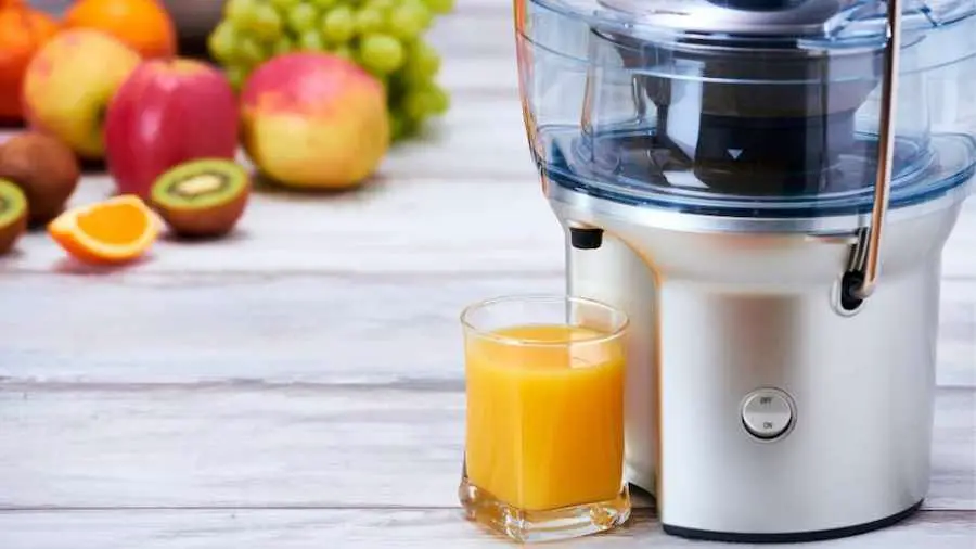 A glass of orange juice sitting near a centrifugal juicer