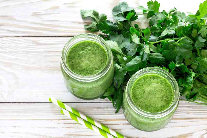 Two green juice jars surrounded with leafy greens