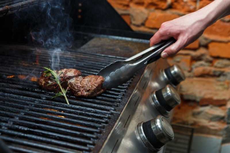 Two pieces of beef cooking on a gas grill 