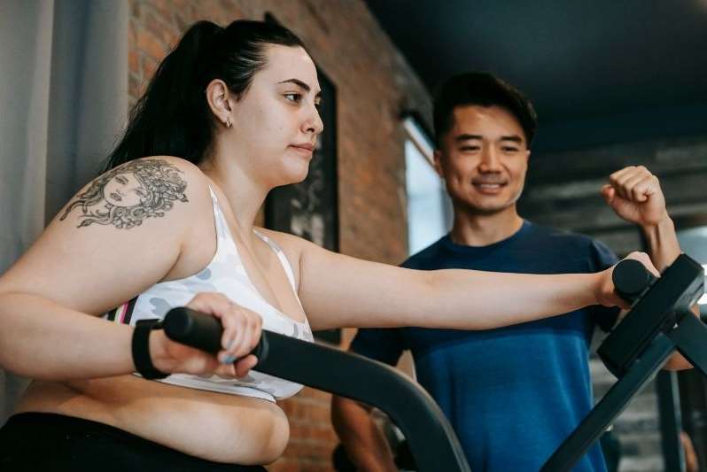 A determined overweight lady doing elliptical training with a personal trainer 