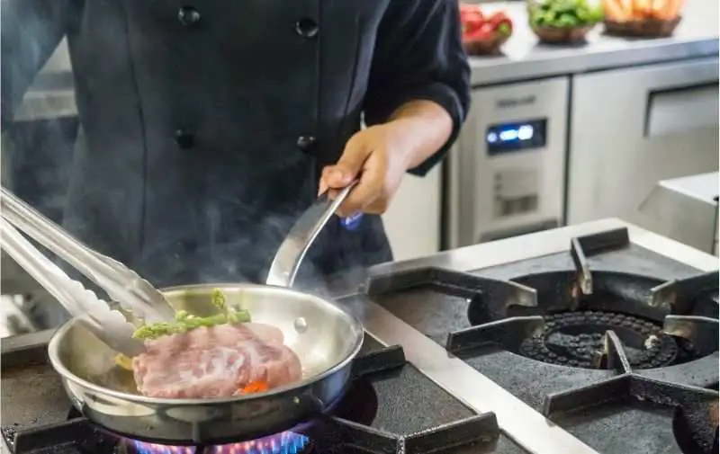 A chef cooking steak on a professional gas range at home