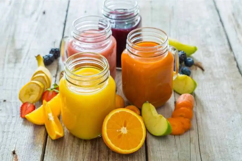 Four jars of juice surrounded with fresh fruit
