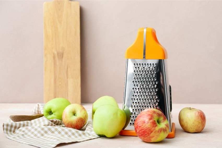 A standard grater and some apples on the kitchen counter 