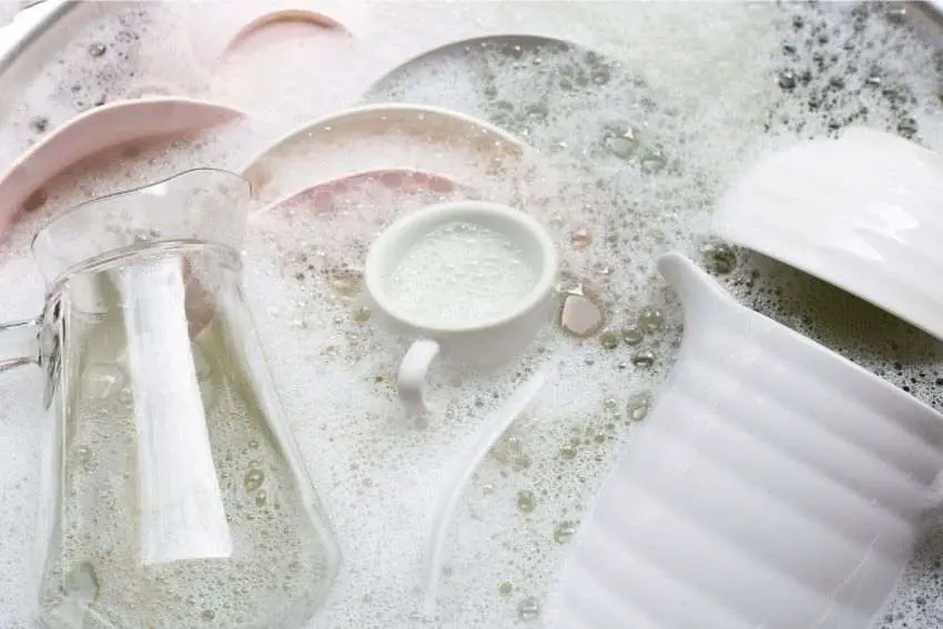 A sink full of various dishes dipped in soapy water 