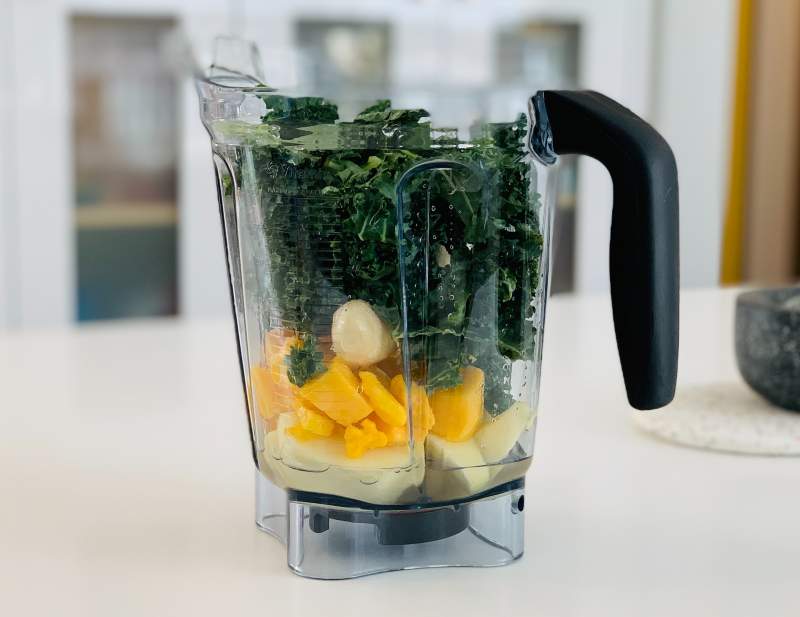 A blender jar full of furits and veggies 