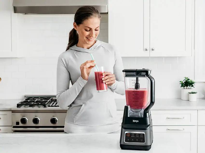 A woman using a Ninja blender to make a red smoothie