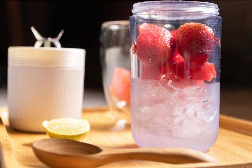 A portable blender container full of strawberries and ice 