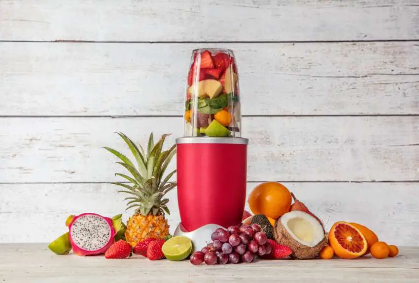 A slim blender surrounded with all sorts of colorful fruits