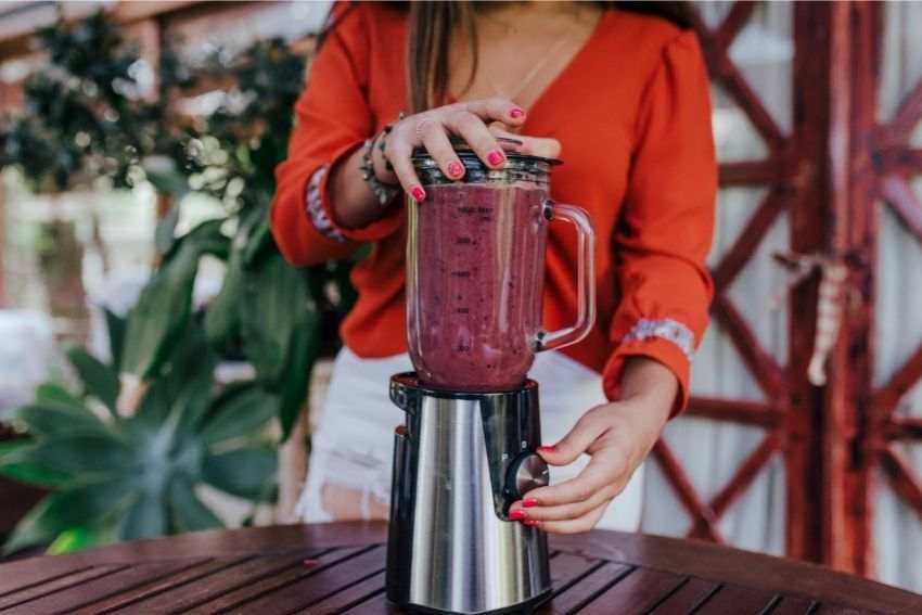 A lady making a red slushie using a blender 