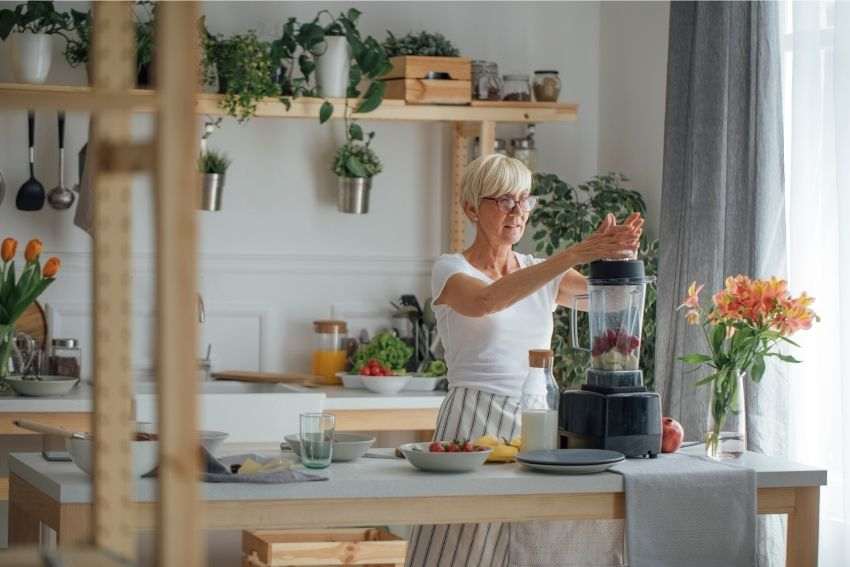 A senior lady making a smoothie with a blender in the kitchen