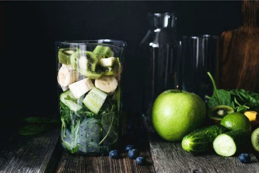 A blender cup full of kiwi, cucumbers, bananas, and healthy greens