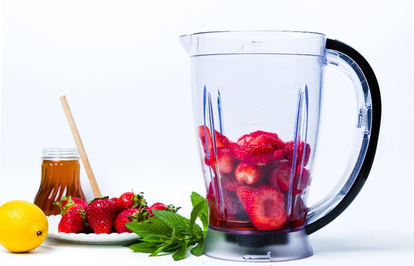 A large blender pitcher full of strawberries 