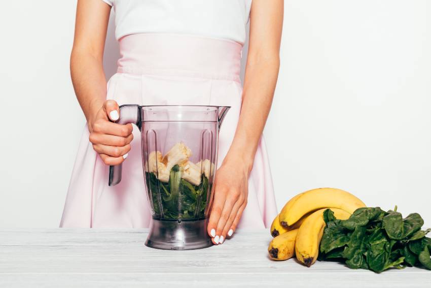 A woman getting ready to blend a green banana smoothie 