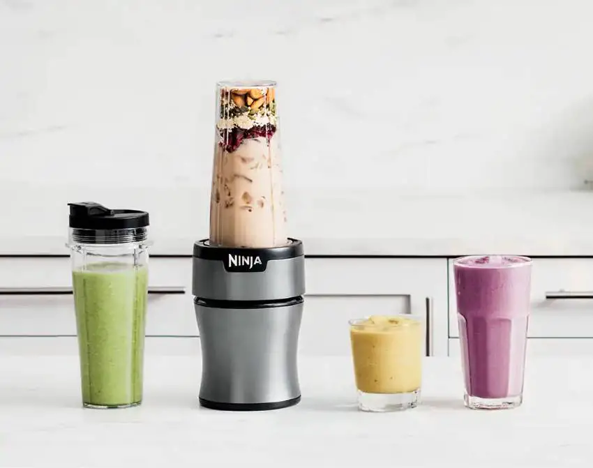A full Ninja blender and some smoothies on the counter 