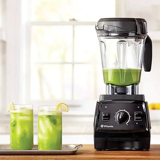 A vitamix blender with a couple of glasses full of green juice