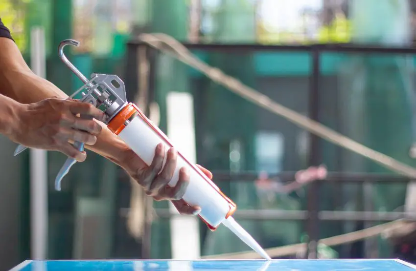 Hands holding a sealant cartridge gun and applying sealant