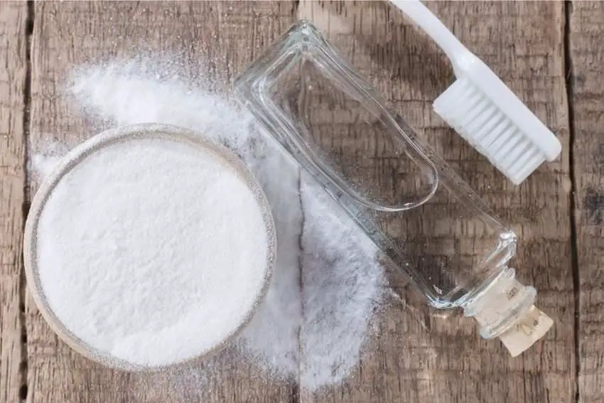 Baking soda, vinegar, and a cleaning brush on a table