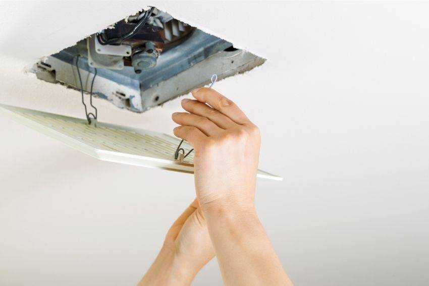 A pair of hands changing the bathroom exhaust fan 