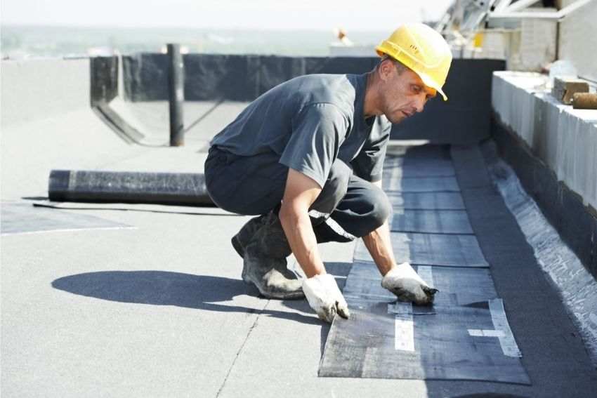 A construction worker laying down protective layers on the roof