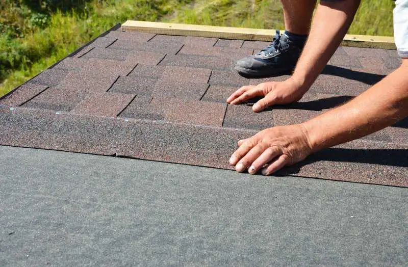 A worker lays new shingles on the protective roof underlayment 