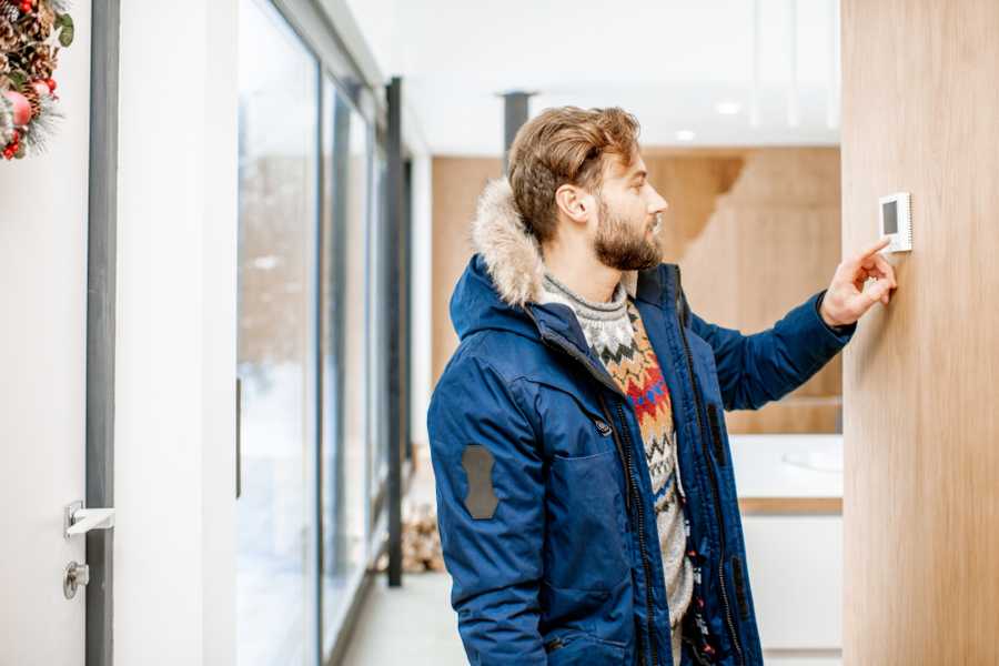 man is adjusting room temperature using thermostat for electric furnace