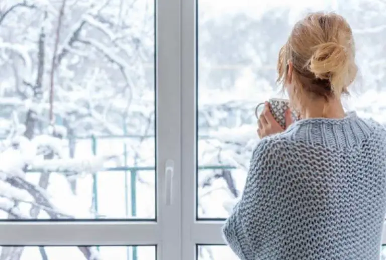 Woman drinking coffee while looking outside on a snowy day using auxiliary heat