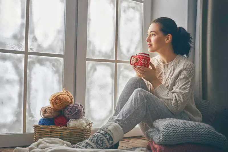 Woman siting near window, drinking a hot cup of tea with auxiliary heat on