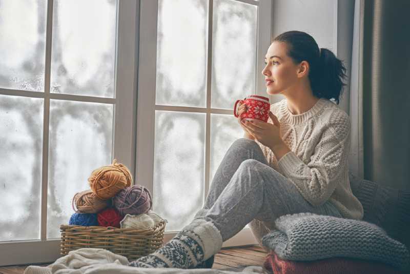 Woman siting near window, drinking a hot cup of tea with auxiliary heat on